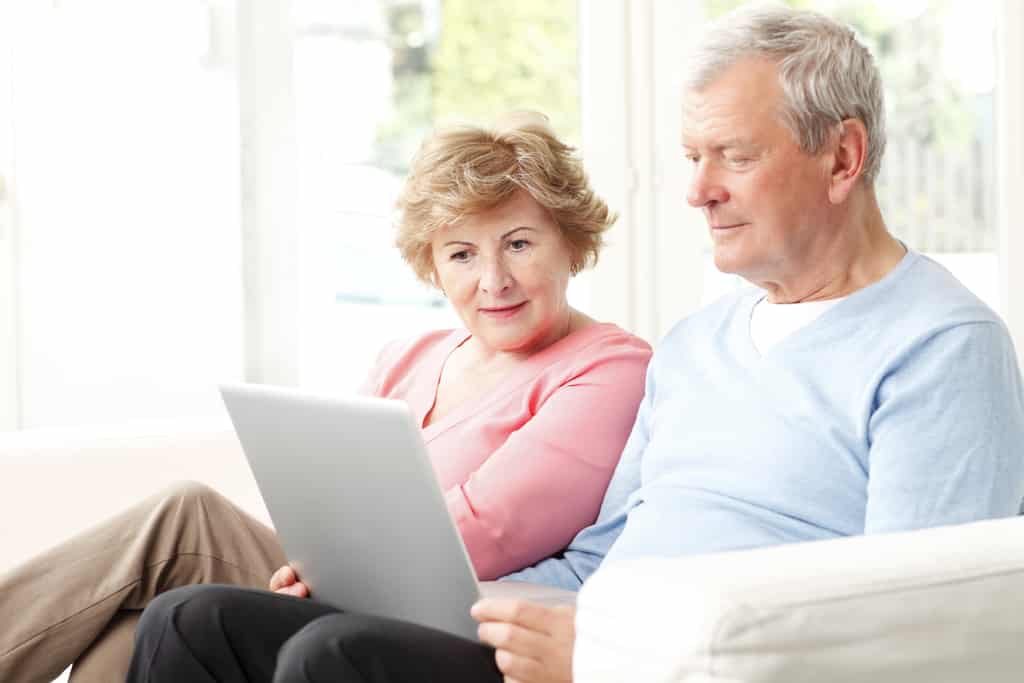 Feliz pareja de ancianos planeando leer en una laptop en casa