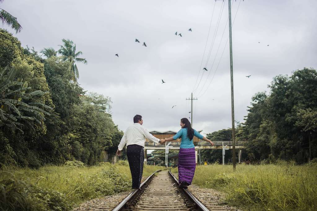 couple with back to camera walking along train tracks holding hands