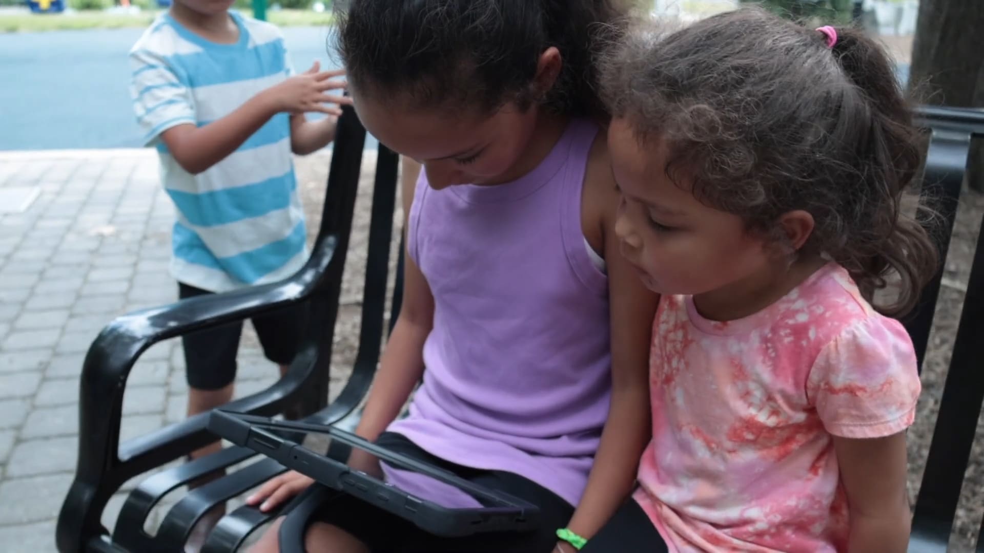 Girl uses her Lingraphica AAC device to communicate with her siblings on the playground.